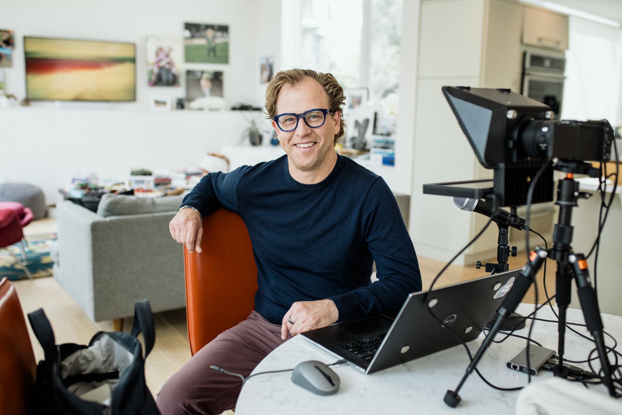 Justin Wolfers in his home setup, smiling at the camera with laptop and teleprompter rig visible.